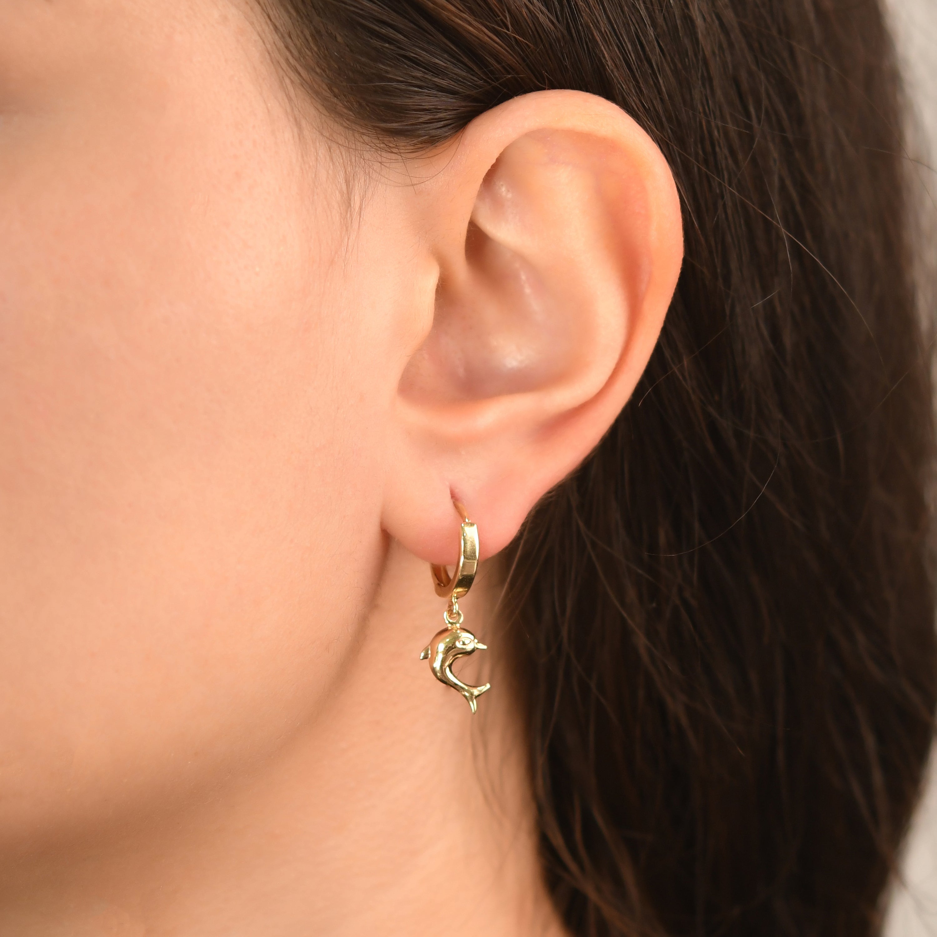 Close-up of 14ct gold hoop earrings with dolphin charm on model's ear.