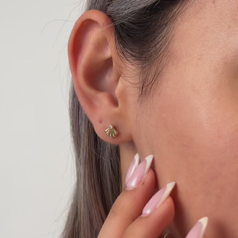Close-up video of an ear with a gold earring, hand adjusting it, on a neutral background