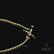 Sleek Kolié 9ct yellow gold bracelet featuring a horizontal cross, a modern twist on a classic design, set against a stark white background. View this piece and more at www.kolie.co.uk.