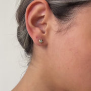 Close-up video of an ear wearing a gold earring with a clear gemstone, against a neutral background.