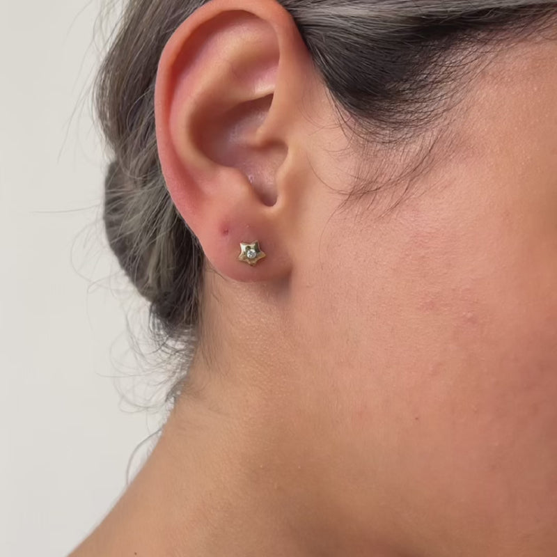 Close-up video of an ear wearing a gold earring with a clear gemstone, against a neutral background.